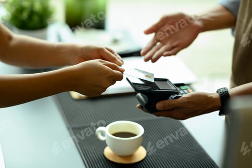 Preview: Close up shot costumer handing a credit card for contactless payment in a modern cafe