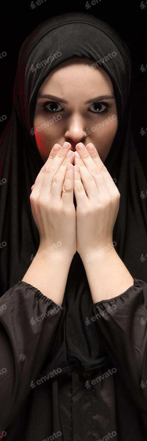 Preview: Portrait of beautiful serious young muslim woman wearing black hijab with hands near her face as