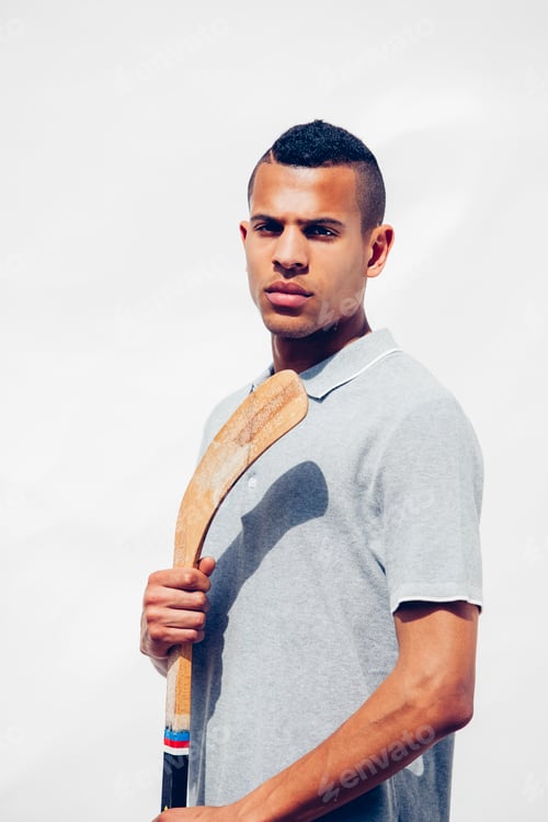 Preview: Portrait of serious looking young man with shaved hair holding hockey stick in front of white backgr