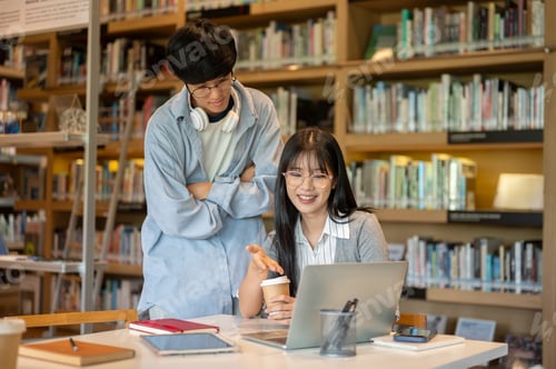 Preview: Glasses asian man student cross arms standing behind woman friend looking at laptop on library table