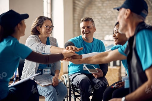 Preview: Multiracial group of happy volunteers stacking their hands in unity while working at aid center.