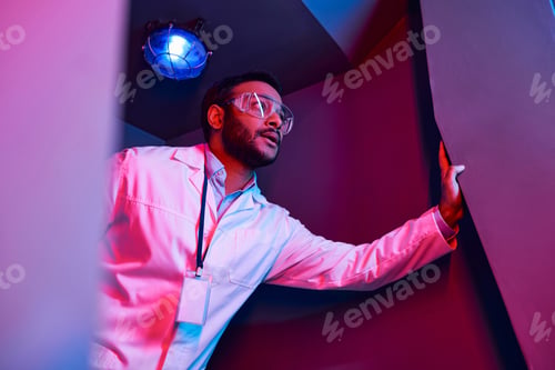 Preview: unknown phenomenon, tense indian scientist looking away in neon-lit science center