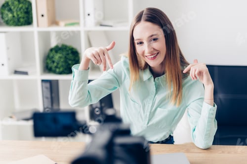 Preview: smiling attractive female video blogger recording vlog and gesturing in office