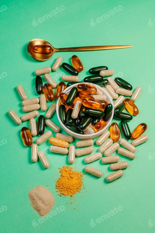 Preview: Green tabletop with an array of vitamin supplement capsules and pills and a spoon