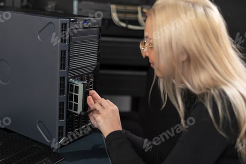 Preview: Female IT technician in their 20s working on a server rack in a data center