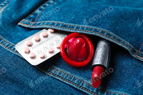 Preview: Red lipstick with condom and birth control pills in pocket of jeans, closeup. Safe sex concept