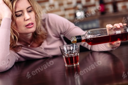 Preview: woman pouring alcohol into glass while sitting at table in kitchen