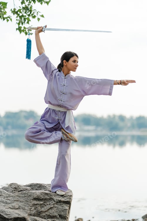 Preview: Kungfu master woman wearing kimono holding sword, practicing wushu standing on stone