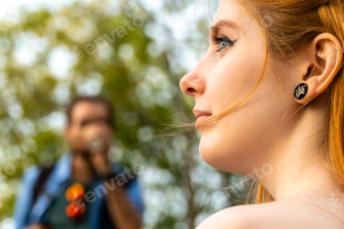 Preview: Pensive young woman looking away against blurred boyfriend drinking takeaway coffee