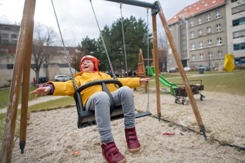 Preview: Happy little girl with Down syndrome on swing outdoors in playgraound.