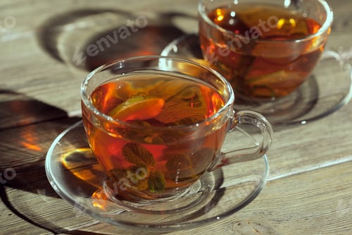 Preview: Two clear cups filled with tea and mint leaves sit on a wooden table in warm light