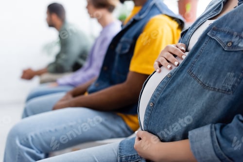 Preview: cropped view of pregnant woman touching belly while sitting in line with blurred multiethnic men,