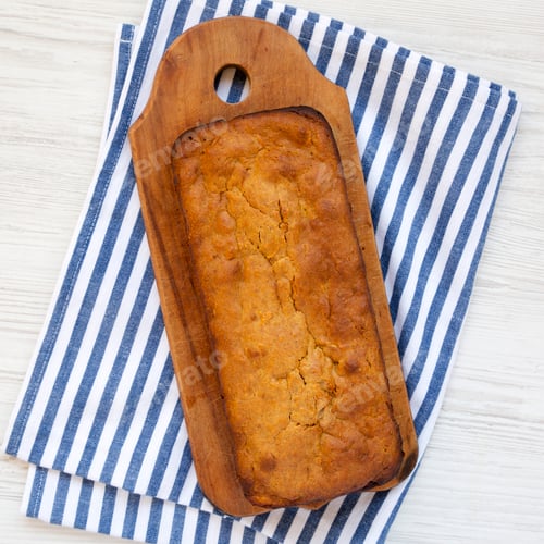 Preview: Homemade Pumpkin Loaf Bread on a rustic wooden board on a white wooden background, top view.