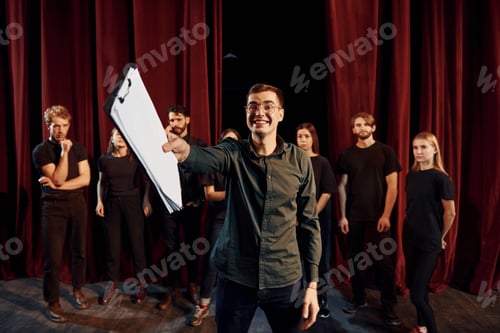 Preview: Man is practicing his role. Group of actors in dark colored clothes on rehearsal in the theater