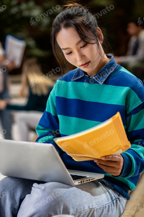 Preview: Portrait of female student siting in campus using laptop.