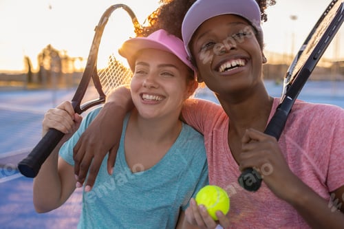 Preview: Two happy multi ethnic female tennis players embracing on a tennis court