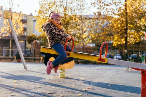 Preview: Autumn playground moment with girl with Down syndrome on seesaw