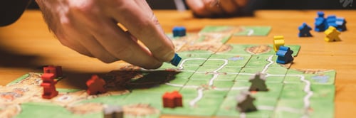 Preview: men friends have fun playing the carcassonne board game at night. male hands and game cards and chip