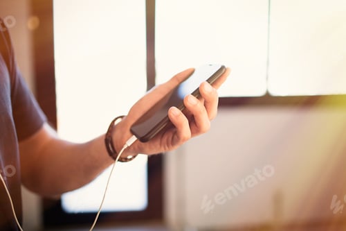 Preview: Handsome bearded guy wearing casual grey t-shirt listening music in earphones, checking social