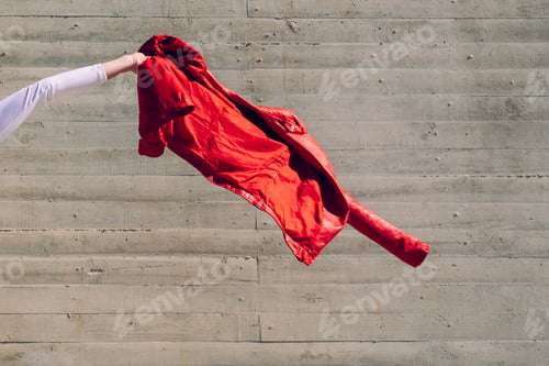 Preview: Arm of young woman waving her red jacket with a gray background copy space.