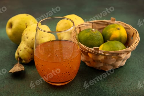 Preview: top view of fresh tangerines on a bucket with quinces and a glass of fresh fruit juice on a green