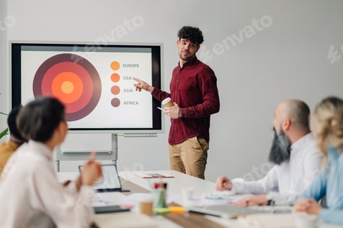 Preview: Young manager pointing at interactive whiteboard during presentation to colleagues in meeting room