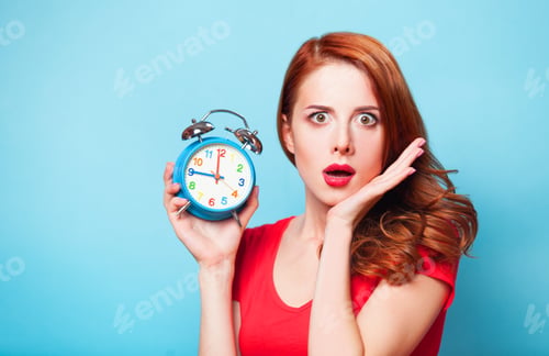 Preview: Redhead girl with alarm clock on blue background.