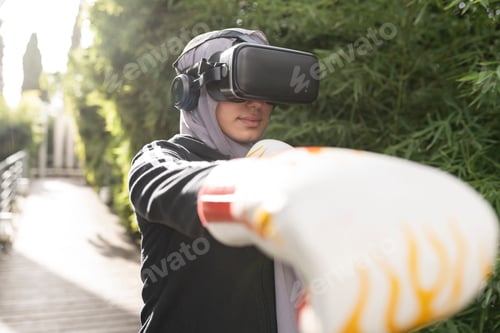 Preview: Unrecognizable arab woman in VR glasses practicing boxing with gloves in park