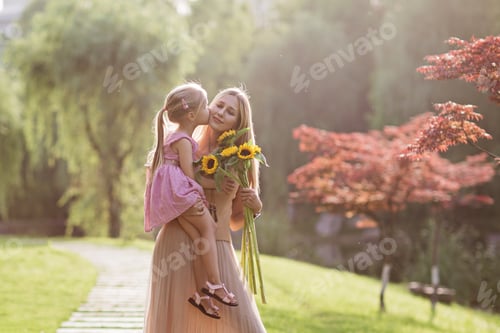 Preview: Portrait of beautiful young caucasian woman and little girl with sunflowers. Kid kissing mommy