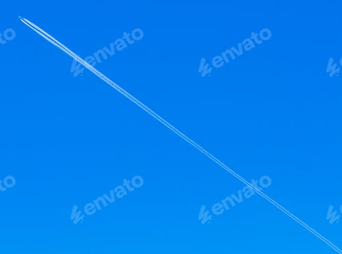 Preview: Low angle shot of a long plane trail in the bright blue summer sky