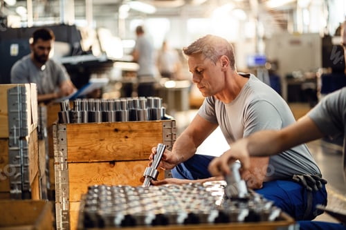 Preview: Manual worker examining manufactured rod cylinders in industrial facility.