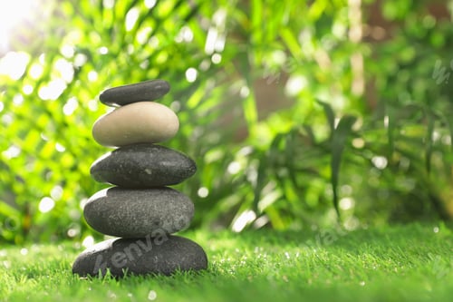 Preview: Stack of stones on green grass against blurred background, space for text. Zen concept