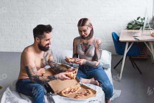 Preview: tattooed couple eating pizza on bed