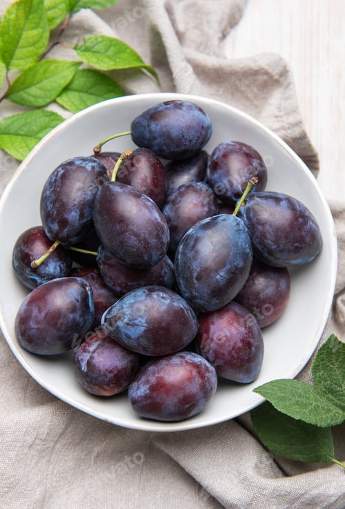 Preview: Fresh ripe plums in white bowl on table