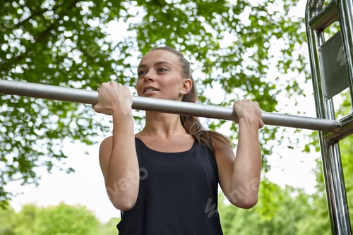 Preview: Young woman training in park, doing chin ups on exercise bars