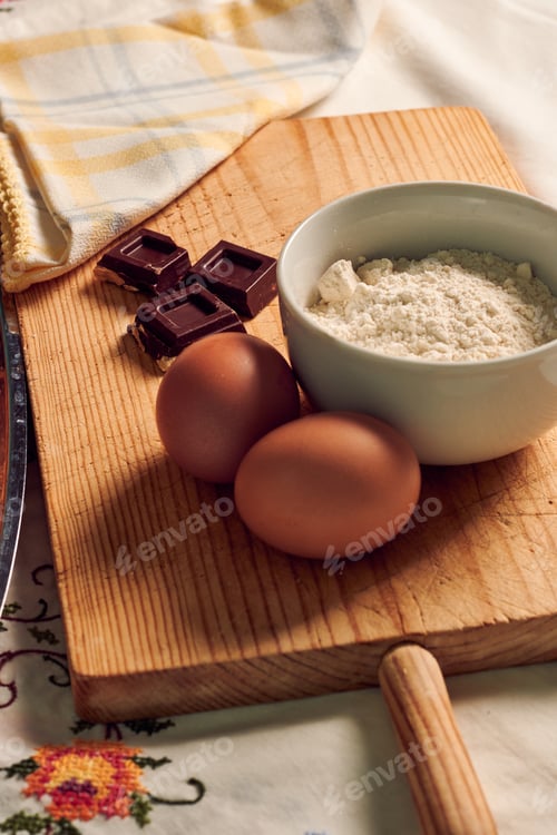Preview: Homemade sponge cake on a white tablecloth with some ingredients: eggs, chocolate and flour