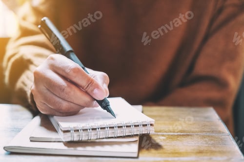 Preview: Closeup image of a woman writing on blank notebook with fountain pen on wooden table