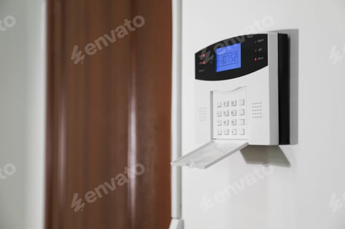 Preview: Home security alarm system on white wall near door, space for text