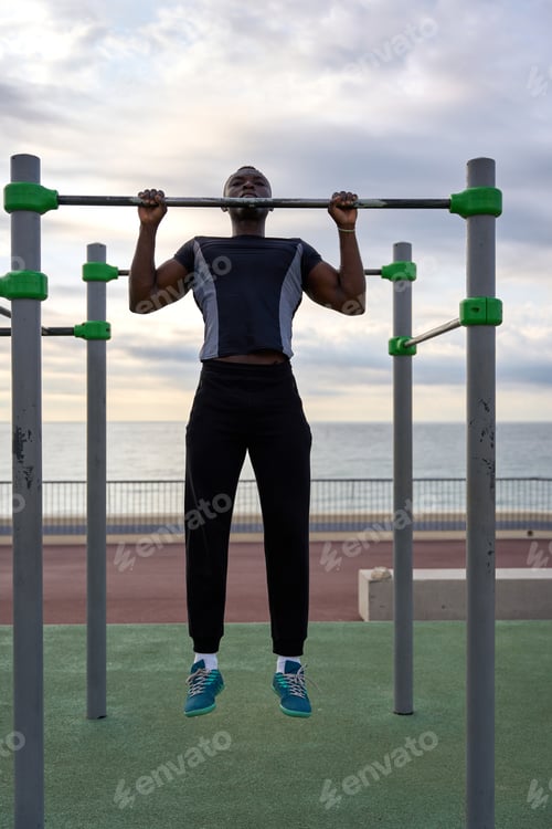 Preview: Young black man performing calisthenics on a horizontal bar by the sea