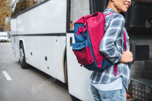 Preview: partial view of female tourist with backpack walking into travel bus at urban srtreet
