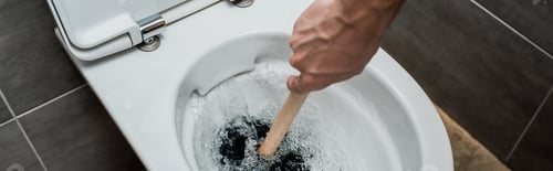 Preview: cropped view of plumber using plunger in toilet bowl during flushing in modern restroom with grey