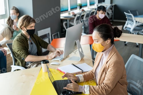 Preview: Group of young co-workers in protective masks working in open space office