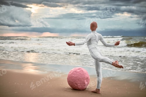 Preview: Hairless performer girl with alopecia in white futuristic suit dancing on sea beach with pink sphere