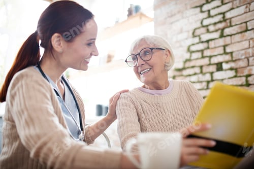 Preview: Red-haired nurse smiling while talking to kind aged woman