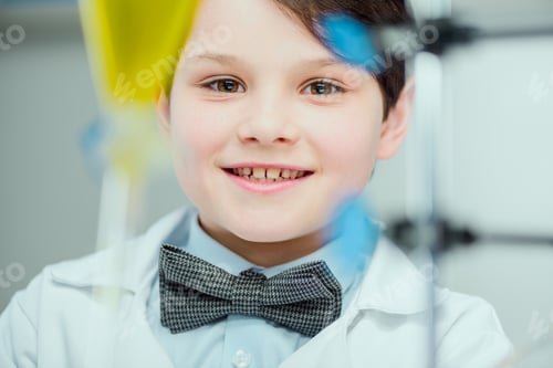 Preview: Close-up portrait of cute smiling schoolboy in lab coat looking at camera, science school concept