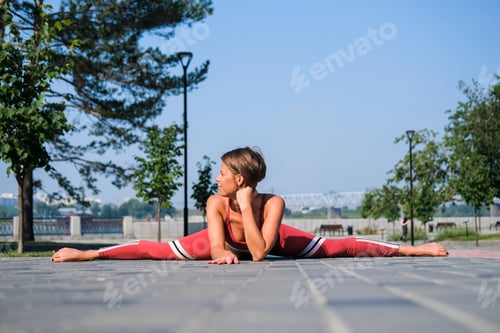 Preview: Young Attractive Woman In Red Sportswear Practices Yoga Exercises Outdoors.