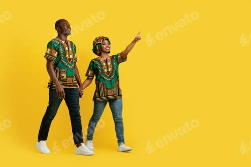 Preview: Cheerful black lovers in african costumes pointing at copy space