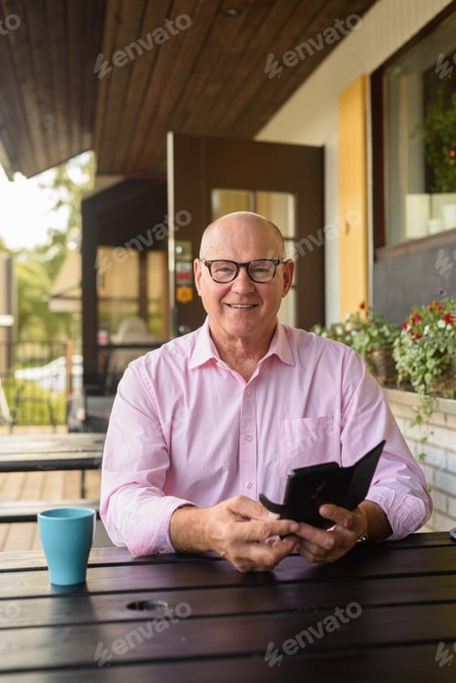 Preview: Happy Senior Man Outdoors in Restaurant Using Mobile Phone