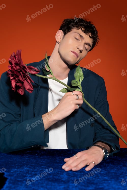 Preview: Trendy man in blue jacket holding dahlia flower isolated on red