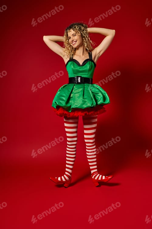 Preview: cheerful new year elf in green festive dress and striped stockings posing with raised arms